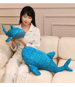 Detail of blue whale shark plush toys with white spots held by a girl on a cozy white sofa