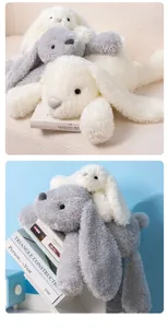 Soft long-eared plush bunny toys in white and grey colors displayed on decorative books.