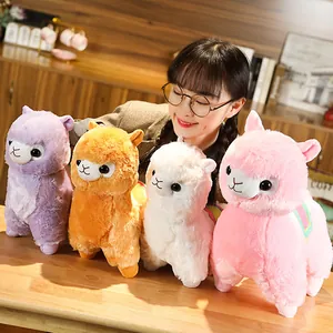 Group of cute colorful alpaca plush toys displayed with a smiling Asian model on a desk