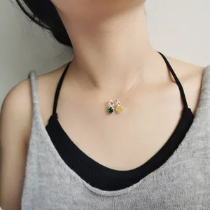 Close-up of small green and yellow gemstone pendants on a thin necklace chain