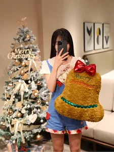 Festliches Weihnachtsglocke-Plüschkissen, gehalten von einem Mädchen im Wohnzimmer.