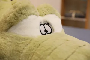 Gros plan du grand coussin en peluche crocodile vert montrant la texture douce et les yeux