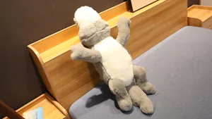 Grande peluche crocodile sur une tête de lit, montrant une fourrure douce grise et blanche.