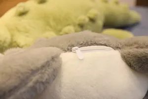 Gros plan du détail de la fermeture éclair blanche sur un oreiller en peluche crocodile.
