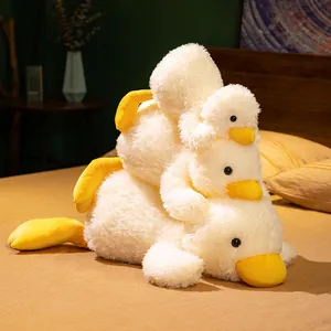 Three stacked cute white and yellow plush ducks in prone position on a cozy bedroom bed