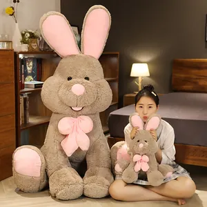 Soft large brown plush rabbit toy with long pink ears and bow, shown with model