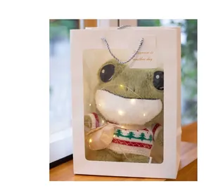 Close-up of cute plush frog in a white gift bag with festive fairy lights decoration