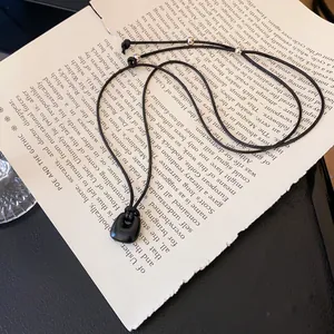 Dettaglio macro della collana con ciondolo nero minimalista su pagine di libro aperto.