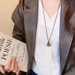 Dettaglio che mostra un ciondolo quadrato marrone minimalista su una lunga collana.