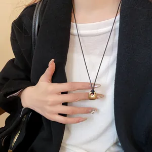 Primo piano di una collana minimalista con ciondolo quadrato dorato indossata da una modella.