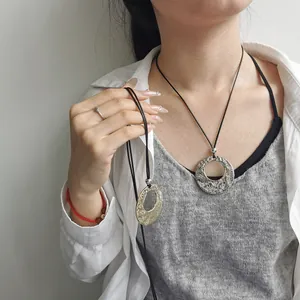 Dettaglio di una collana etnica con pendente in metallo stropicciato su cordino in cuoio