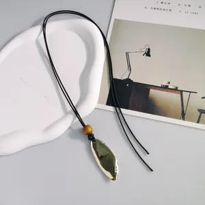 Primo piano di una collana lunga in stile etnico con ciondolo dorato stropicciato.