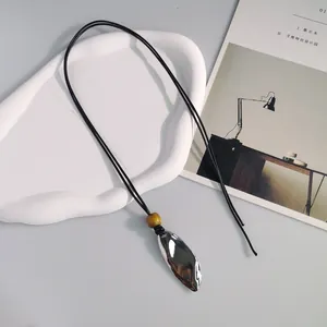 Primo piano di una collana in pelle minimalista con ciondolo metallico ovale stropicciato.