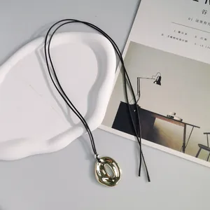 Primo piano di un ciondolo ovale stropicciato in oro su una collana in cordino nero