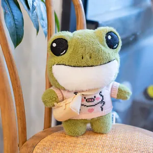 Cute green frog plush toy wearing pink sweater and crossbody bag on wooden chair