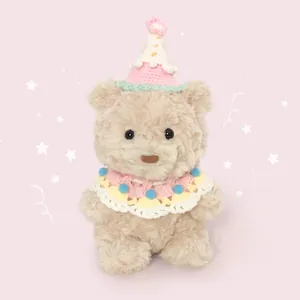 Cute beige plush teddy bear wearing a knitted birthday hat and collar on pink background.