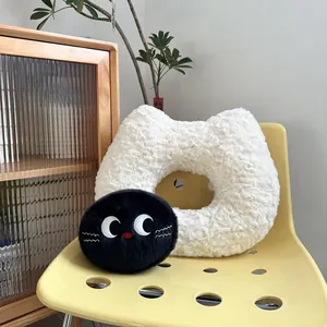 Cute cat-shaped plush doughnut cushion and black round pillow on yellow chair