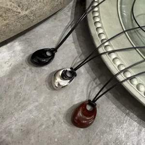 Detailansicht von drei Tropfenanhängern in Schwarz, Silber und Braun an schwarzen Kordeln