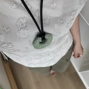Detalle de un collar con colgante redondo de piedra de lava verde y cordón negro para mujer