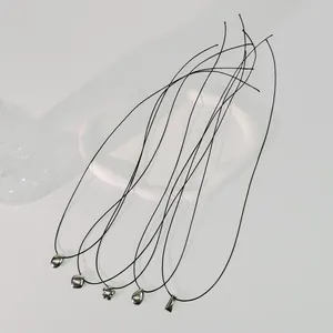 Detailansicht mehrerer schwarzer Wachskordel-Halsketten mit silbernen geometrischen Anhängern.