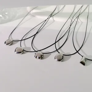 Nahaufnahme verschiedener silberner Metallanhänger an schwarzen Wachskordel-Choker-Halsketten