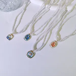 Detailansicht französischer Vintage-Perlenketten mit bunten Emaille-Blumenanhängern.