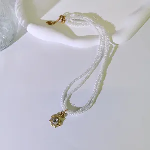 Detailansicht einer dreireihigen Kunstperlenkette mit einem goldenen Blumenanhänger