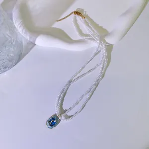 Detailansicht einer zweireihigen Perlenkette mit blauem Emaille-Blumenanhänger