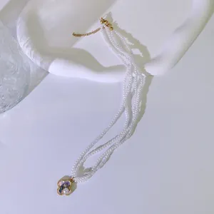 Nahaufnahme einer dreireihigen Perlenkette mit lila emailliertem Blumenanhänger