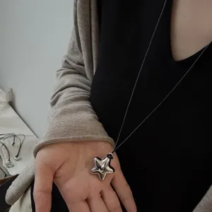 Makroansicht eines minimalistischen silbernen Sternanhängers an einer langen schwarzen Kette.