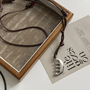 Macro view of a creative stainless steel comb pendant necklace with a brown cord.