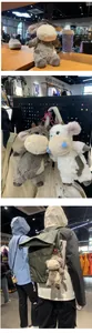 Plush cow doll keychain pendant hanging on an olive backpack in a store setting