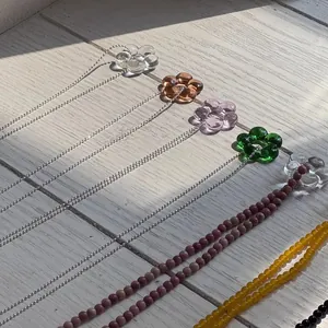 Dettaglio di collane con fiori in vetro colorato e varie catene di perline su superficie in legno