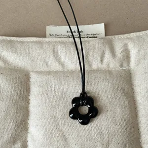 Vista dettagliata del ciondolo a fiore in vetro nero lucido su un cordino minimalista