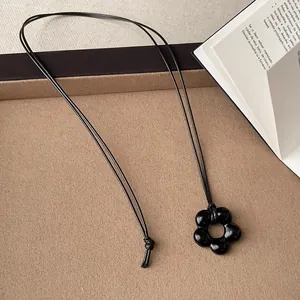 Primo piano del ciondolo a fiore nero in vetro su una collana a corda lunga minimalista