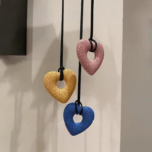 Detail view of three textured volcanic stone heart pendants hanging on black leather cords