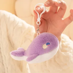 Soft purple plush whale keychain pendant held by hand against a warm knitted background