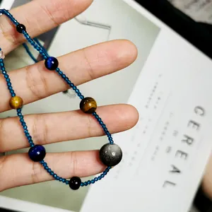 Detailaufnahme einer blauen Perlenkette mit Tigerauge-Steinen, in der Hand gehalten