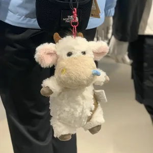 Creative fluffy plush cow doll bag charm with pink hook, attached to a backpack strap