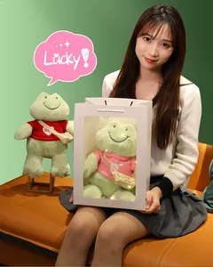 Peluche de rana verde sonriente sostenido por modelo asiática en bolsa de regalo
