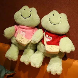 Dos lindos peluches de ranas verdes sonrientes con suéteres de colores y bolsos pequeños.