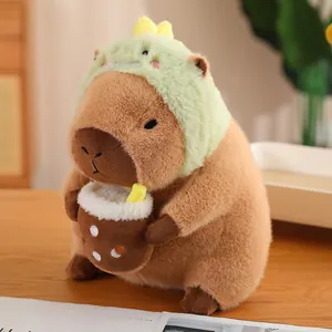 Adorable capybara plush toy wearing a green dinosaur hood holding a milk tea cup