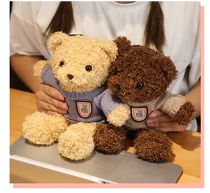 Two small plush teddy bears wearing cozy knitted sweaters held over a laptop.
