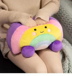 Soft rainbow plush hand warmer pillow used by a person in a cozy home setting