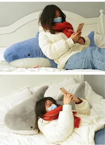 Large soft shark plush toy used as a comfortable and fluffy body pillow on a bed.