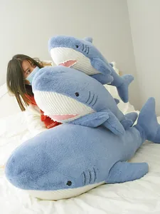Set of three soft blue shark plush toys in various sizes stacked on white indoor bedding