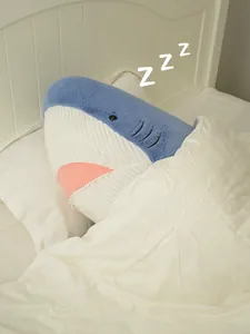 Detail showing a cute blue shark plush toy sleeping tucked into a cozy white bed