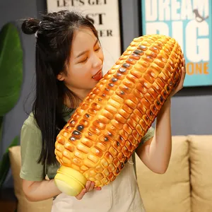 Giant realistic grilled corn plush pillow held by a model in a cozy home setting.