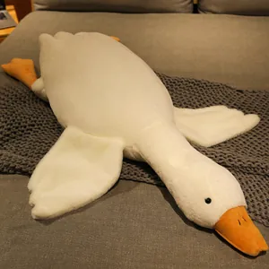 Grand coussin peluche oie blanche douce reposant sur une couverture tricotée grise