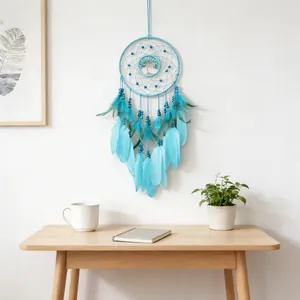 Turquoise tree of life dreamcatcher with feathers hanging on a white wall above a wooden table